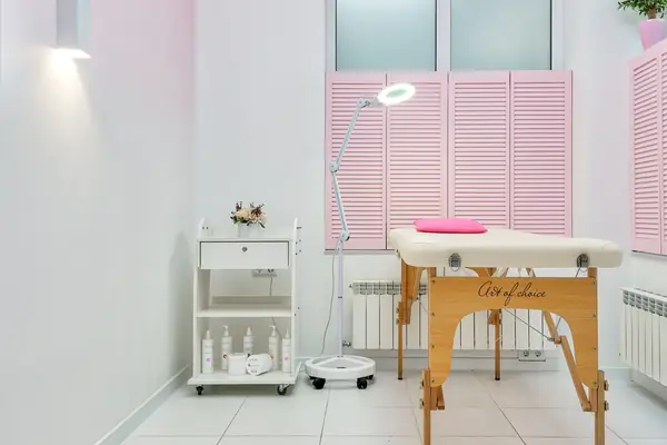 Een lichte behandelkamer met een behandeltafel, een loeplamp en roze luiken
