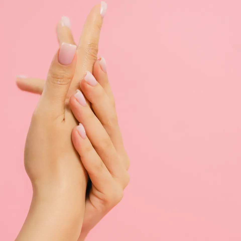 Twee handen met verzorgde nagels in zacht roze licht